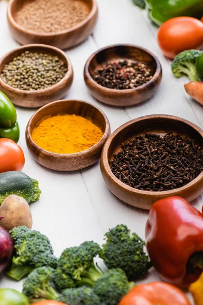 Selective focus of fresh ripe vegetables and fruits around bowls with spices on wooden white background — Stock Photo