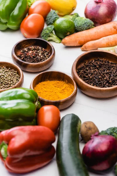 Selective focus of fresh ripe vegetables and fruits around bowls with spices on wooden white background — Stock Photo