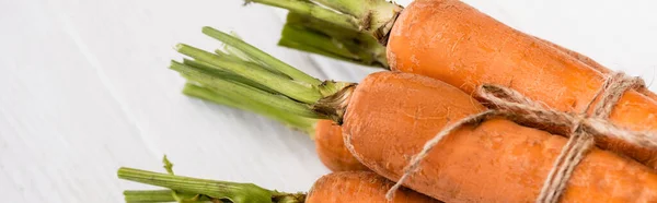 Close up view of fresh carrots tied with rope on white wooden table, panoramic shot — Stock Photo