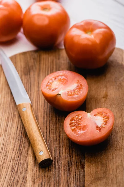 Enfoque selectivo de tomates maduros sobre tabla de cortar de madera con cuchillo - foto de stock