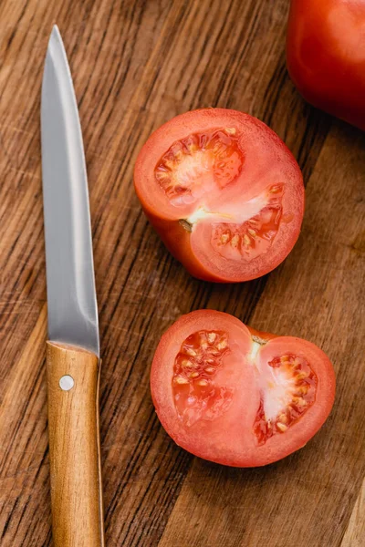 Vista superior de mitades de tomate maduro sobre tabla de cortar de madera con cuchillo - foto de stock