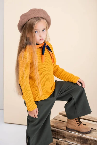 Menina loira na moda em roupa de outono posando na caixa de madeira no fundo bege e branco — Fotografia de Stock