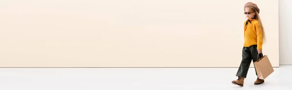 Модная блондинка в осеннем наряде и солнцезащитных очках прогулка с сумкой для покупок на бежевом и белом фоне, панорамный снимок — стоковое фото