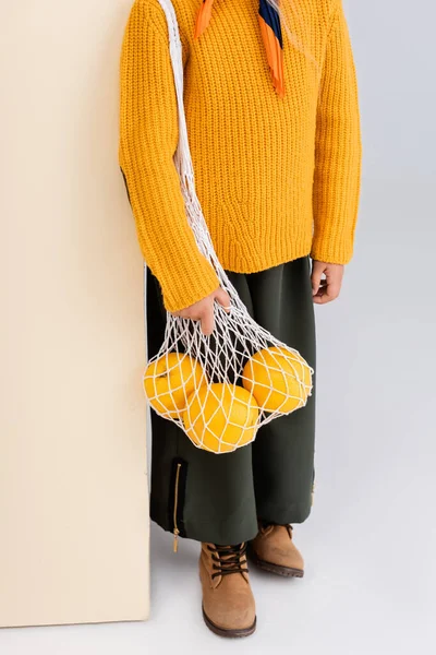 Vista recortada de chica de moda en traje de otoño posando con pomelos en bolsa de hilo sobre fondo beige y blanco - foto de stock