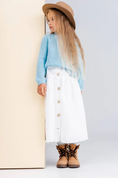 Fashionable blonde girl in brown hat and boots, white skirt and blue sweater near beige wall — Stock Photo