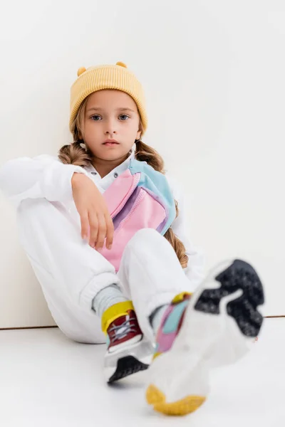 Enfoque selectivo de chica rubia en ropa deportiva sentado cerca de la pared blanca - foto de stock