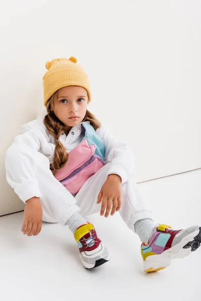 Chica rubia en ropa deportiva sentado cerca de la pared blanca - foto de stock