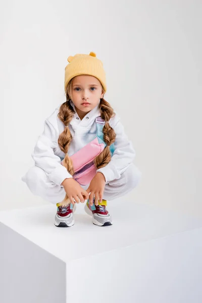 Menina loira em sportswear sentado no cubo isolado no branco — Fotografia de Stock