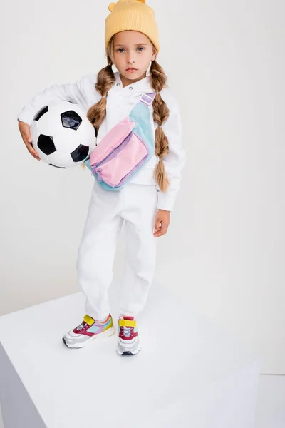 Блондинка в спортивному одязі, що стоїть на кубі з футбольним м'ячем ізольована на білому — стокове фото