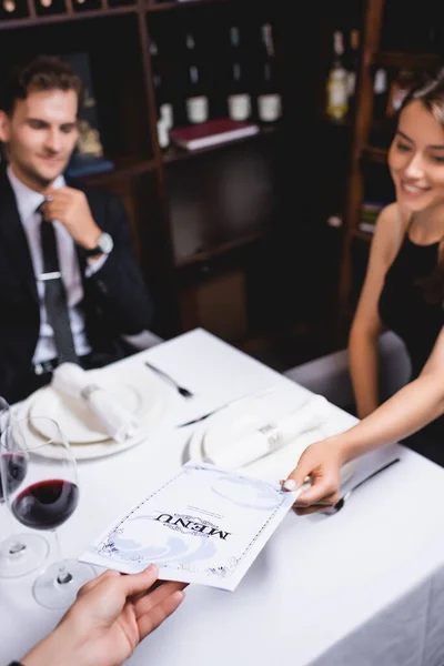 Foco seletivo de garçons que dão cardápio à mulher à mesa no restaurante — Fotografia de Stock