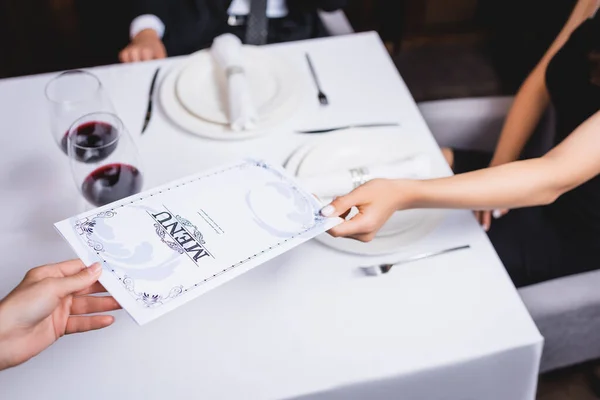 Обрезанный вид официантки, дающей меню молодой женщине в ресторане — стоковое фото