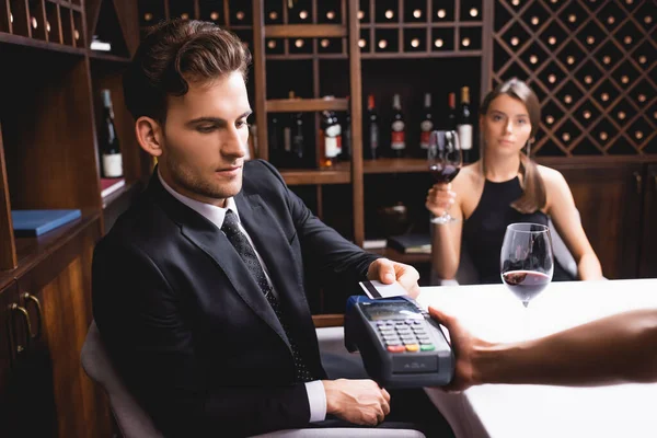 Selective focus of man with credit card paying to waitress with payment terminal during dating with girlfriend in restaurant — Stock Photo