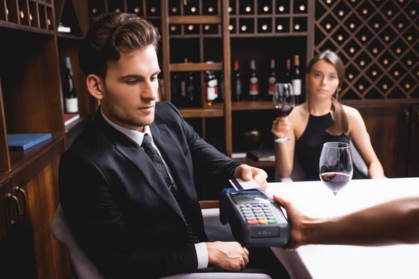 Enfoque selectivo del hombre con tarjeta de crédito que paga a la camarera con terminal de pago durante las citas con su novia en el restaurante - foto de stock