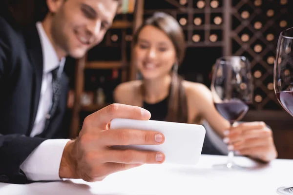 Selective focus of young couple looking at smartphone near glasses of wine in restaurant — Stock Photo