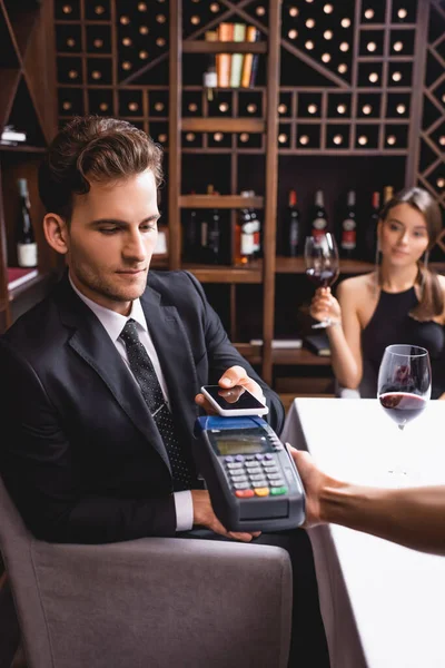 Selektiver Fokus der Kellnerin mit Zahlungsterminal in der Nähe von Mann mit Smartphone im Restaurant — Stockfoto