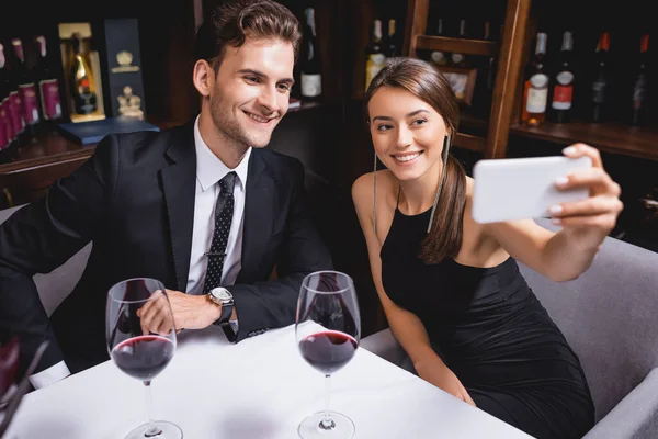 Enfoque selectivo de pareja joven tomando selfie cerca de copas de vino en restaurante - foto de stock