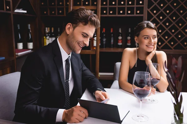 El foco selectivo del hombre mirando el menú cerca de la amiga y las copas del vino en el restaurante - foto de stock