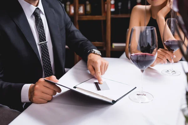 Cropped view of man putting credit card in restaurant bill near glasses of wine and girlfriend — Stock Photo