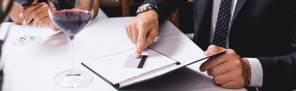 Image horizontale de l'homme mettant la carte de crédit dans la facture du restaurant près de verres de vin et petite amie — Photo de stock