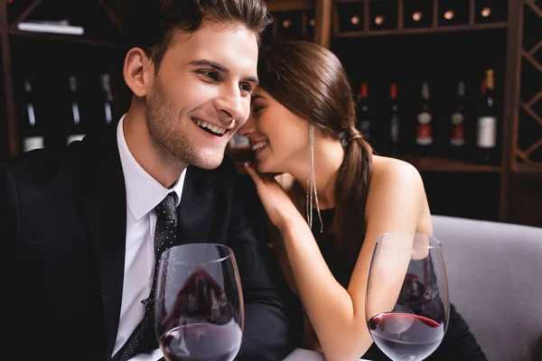 Foco seletivo de mulher elegante abraçando namorado em terno perto de copos de vinho no restaurante — Fotografia de Stock