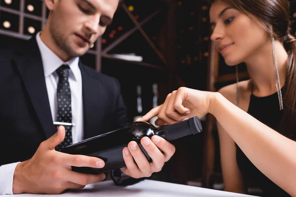 Selective focus of woman pointing at bottle of wine near boyfriend in suit in restaurant — Stock Photo