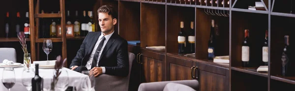 Horizontal image of young man in formal wear sitting near glass of wine on table in restaurant — Stock Photo