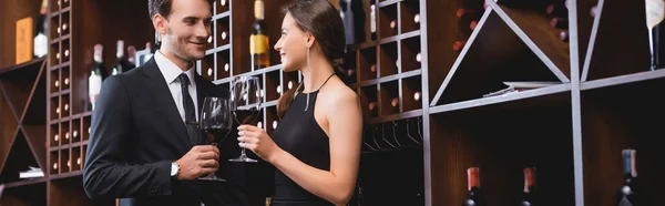 Panoramic shot of elegant couple holding wine glasses and looking at each other in restaurant — Stock Photo