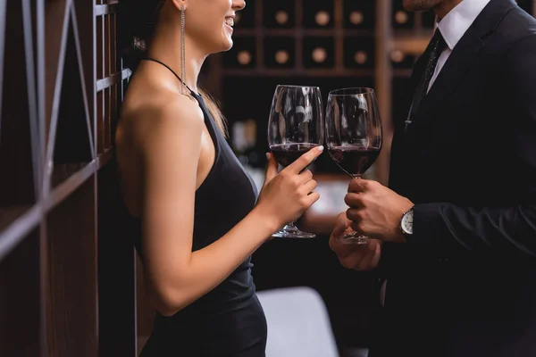 Vista recortada de la elegante mujer sosteniendo copa de vino cerca de novio en traje en el restaurante - foto de stock