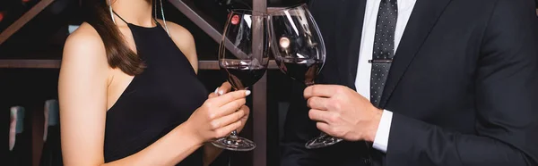 Cultivo panorámico de elegante pareja tintineando con vino en restaurante - foto de stock