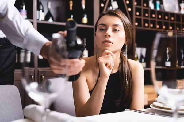 Избранное внимание элегантной женщины, смотрящей на сомелье с бутылкой вина, сидя за сказочным столом в ресторане — стоковое фото