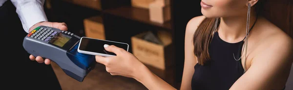 Panoramic crop of woman paying with smartphone to waiter with payment terminal in restaurant — Stock Photo