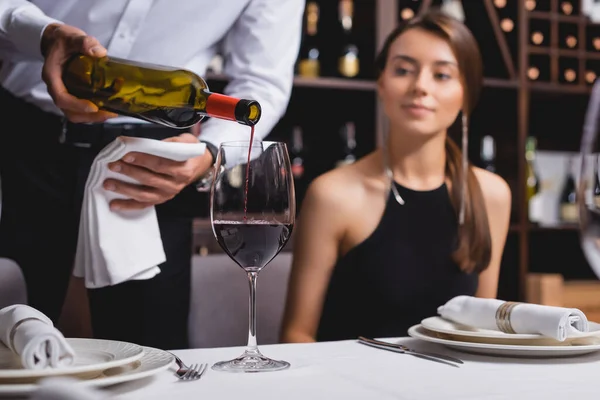 Foco seletivo de vinho sommelier derramando perto da mulher à mesa no restaurante — Fotografia de Stock