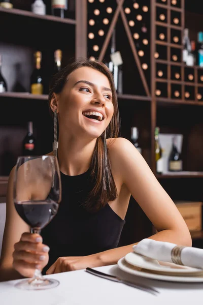 Focus selettivo di una donna elegante che ride mentre tiene in mano un bicchiere di vino nel ristorante — Foto stock