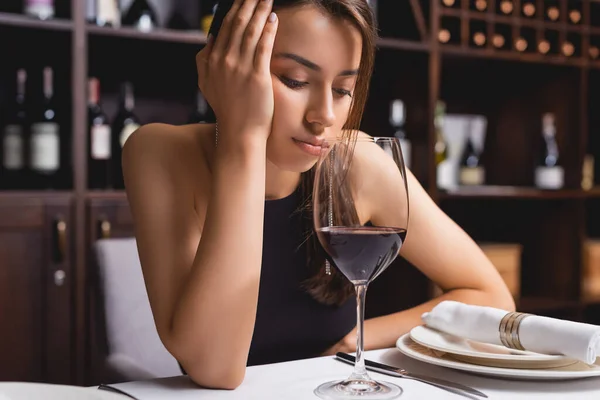 Сумна жінка дивиться на келих вина за столом у ресторані — стокове фото