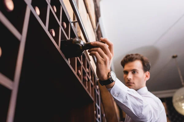 Enfoque selectivo del sommelier tomando botella de vino del estante en el restaurante - foto de stock