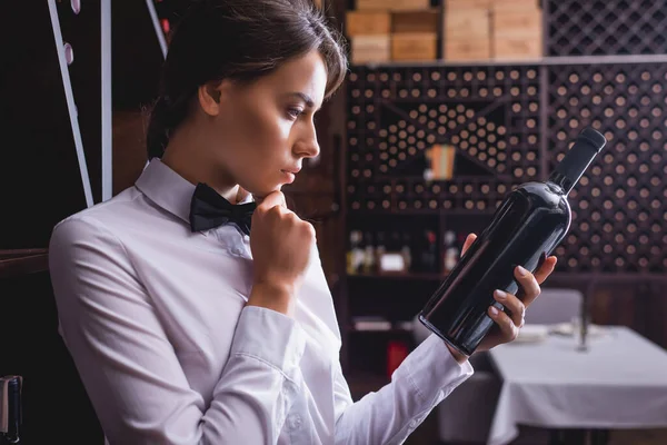 Sommelier pensativo sosteniendo botella de vino en el restaurante - foto de stock