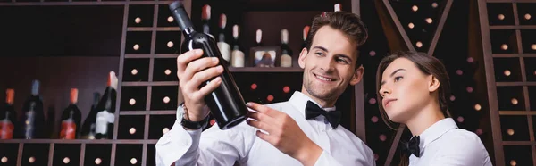Website header of sommelier holding bottle of wine near colleague in restaurant — Stock Photo