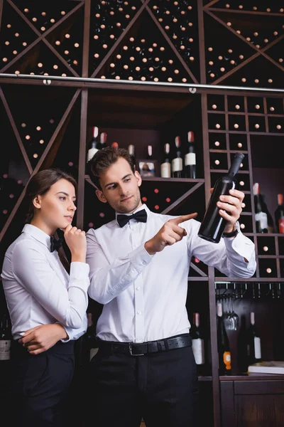 Sommelier zeigt mit Finger auf Flasche Wein neben nachdenklichen Kollegen im Restaurant — Stockfoto