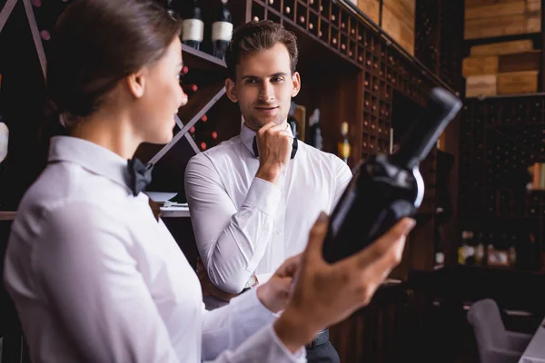 Selective focus of sommelier looking at colleague with bottle of wine in restaurant — Stock Photo