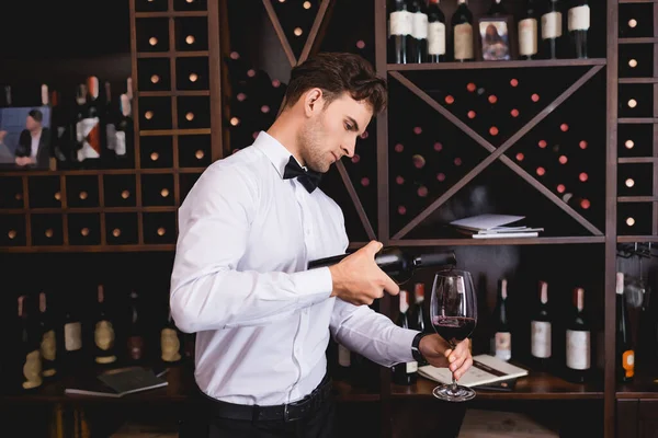 Joven sommelier vertiendo vino en copa en restaurante - foto de stock