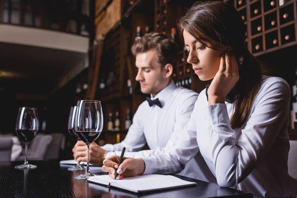 Selective focus of sommeliers writing on notebooks near glasses of wine in restaurant — Stock Photo