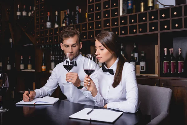 Selective focus of sommeliers smelling wine near notebooks on table — Stock Photo