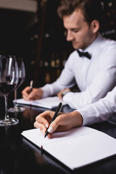 Enfoque selectivo de sommeliers que escriben en cuadernos cerca de copas de vino en la mesa — Stock Photo