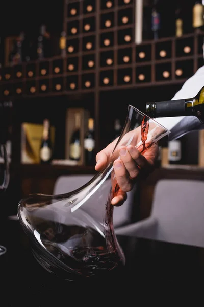 Vista ritagliata del sommelier versando vino rosso in decanter sulla tavola — Foto stock