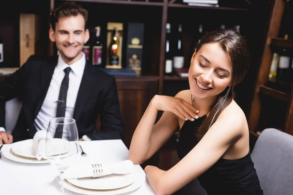 Selective focus of elegant woman with closed eyes sitting near man in suit at table in restaurant — Stock Photo