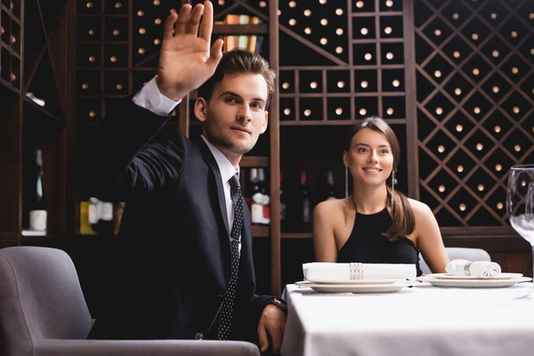 Selektiver Fokus eines Mannes im Anzug, der in einem Restaurant neben einer eleganten Frau winkt — Stockfoto