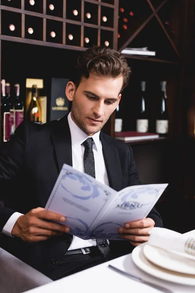 Selective focus of young man in formal wear holding menu in restaurant — Stock Photo
