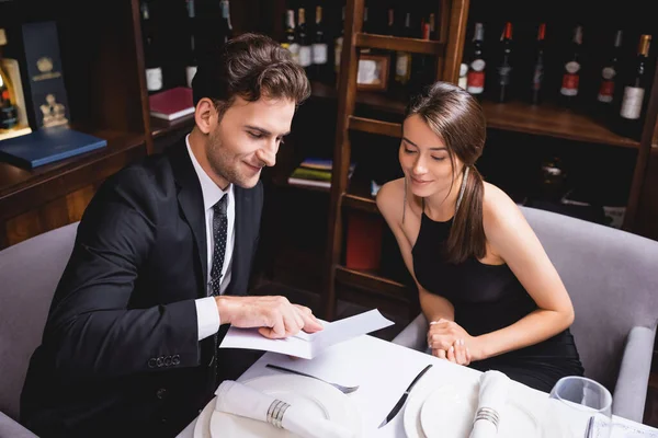 Selective focus of man pointing at menu beside girlfriend in restaurant — Stock Photo