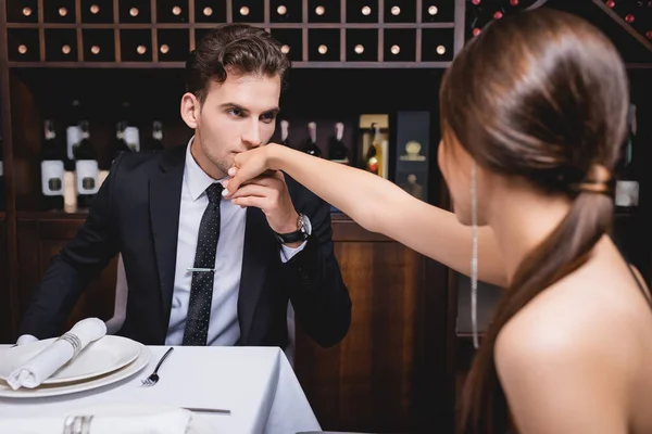 Selective focus of man in formal wear kissing hand of girlfriend during dating in restaurant — Stock Photo