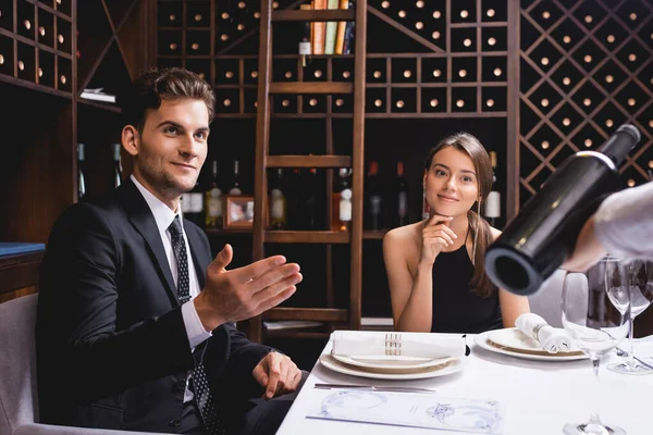 Concentration sélective de l'homme pointant vers sommelier avec bouteille de vin près de petite amie dans le restaurant — Photo de stock